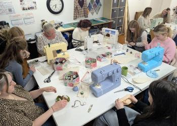Group of people gathered around a table working with sewing machines