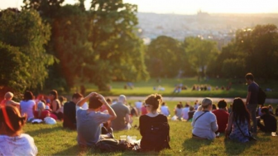 people sitting in a park looking over the city. the sun is setting